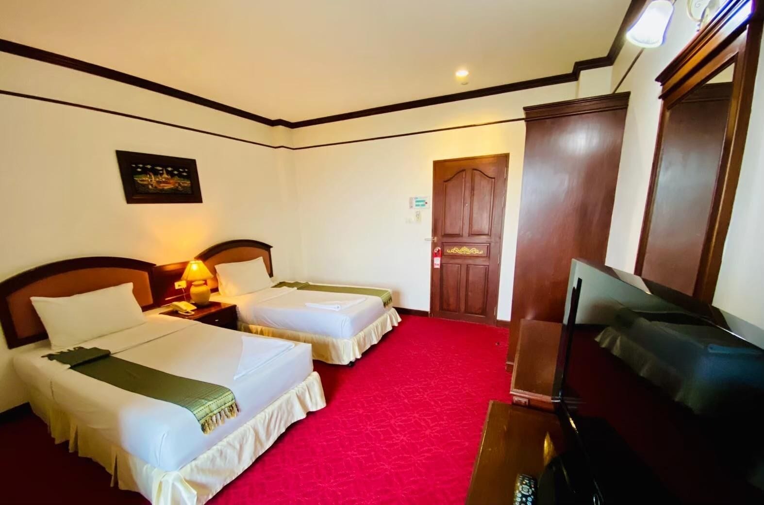 Habitación de hotel con dos camas, un televisor y una alfombra roja.