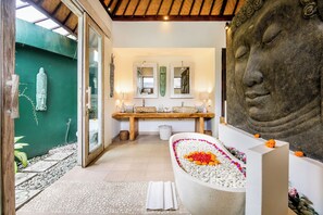 A spa-like bathroom with a large bathtub, a Buddha statue, and a wooden bench. - Villa Balissima (Seminyak)