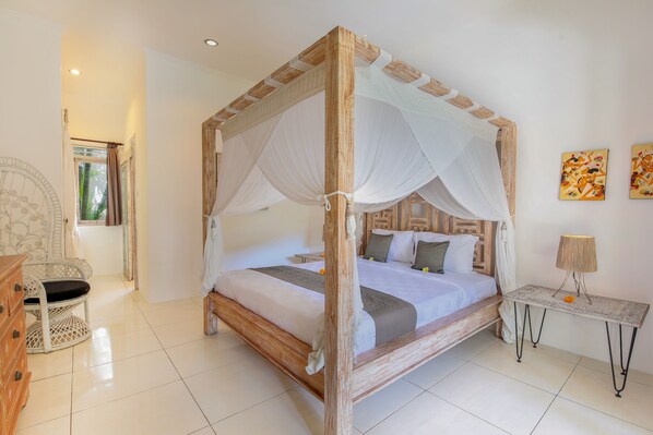 A four-poster bed with a canopy, a bedside table with a lamp, and artwork on the wall. - Villa Balissima (Seminyak)