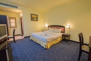 A hotel room with a neatly made bed, a television, a chair, and a small table with a phone. - Pannapa Resort (Krabi)