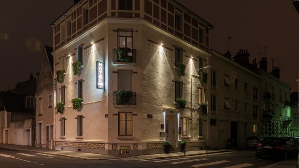Un edificio en esquina con varias ventanas, algunas con plantas, y una entrada visible.