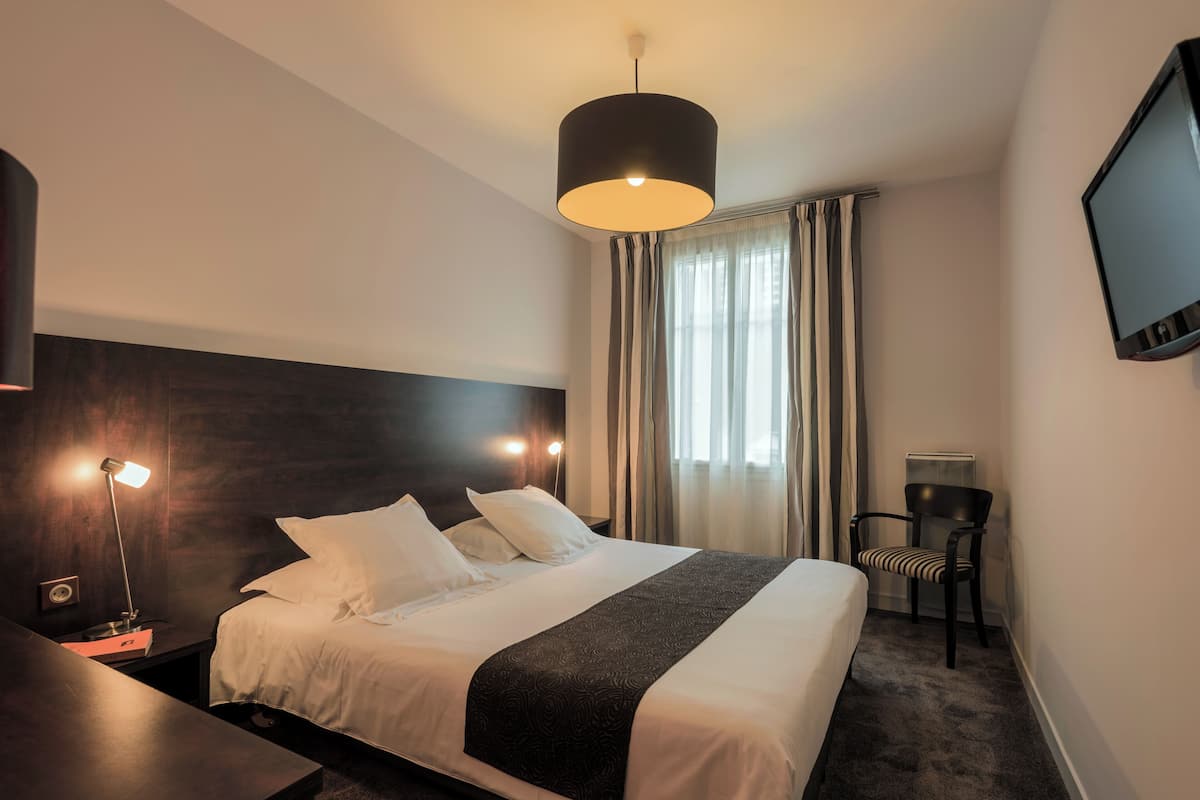 A hotel room with a large bed, a desk, a chair, a TV, and a window with curtains.