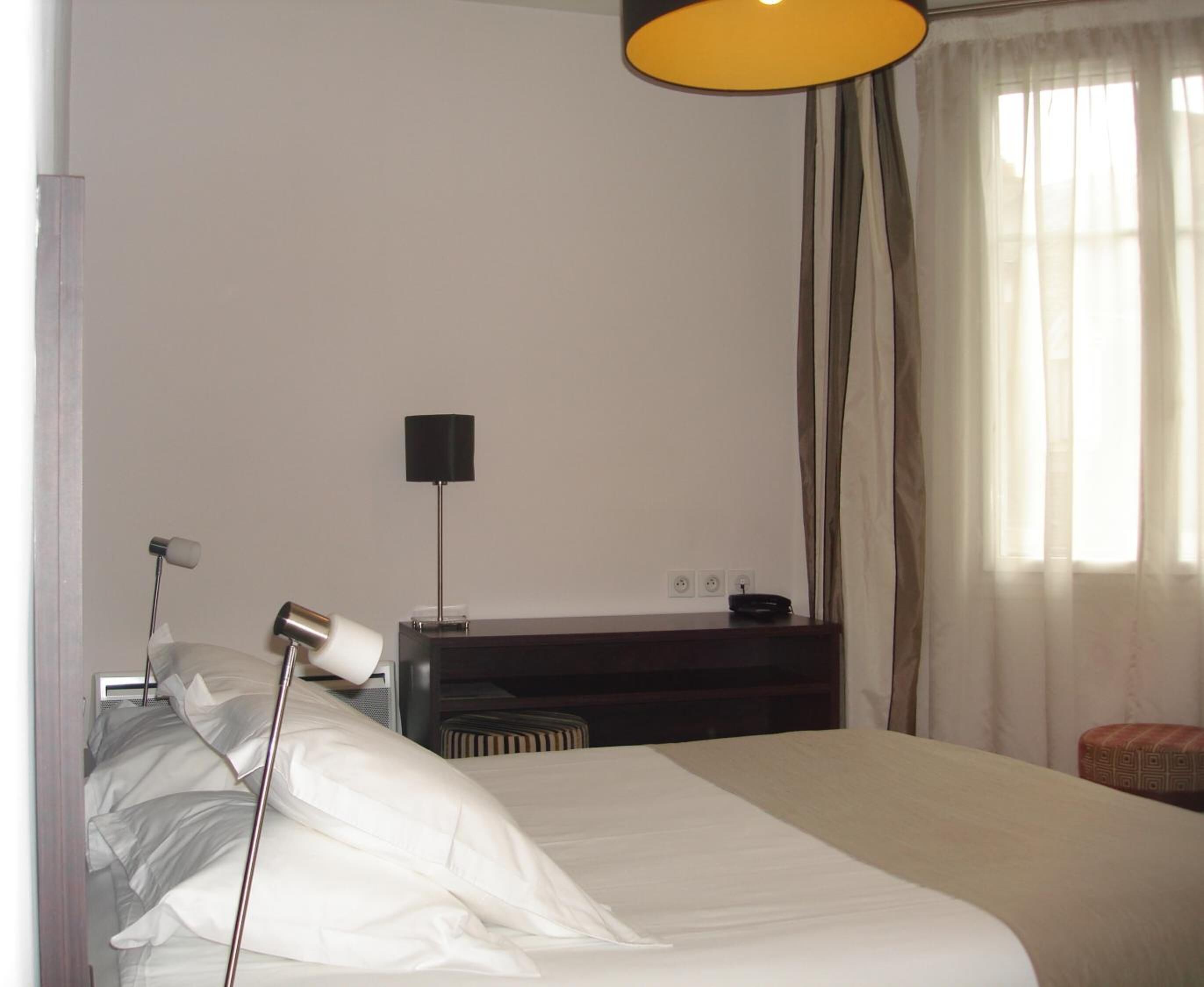 A hotel room with a bed, a desk, a lamp, and a window with curtains.