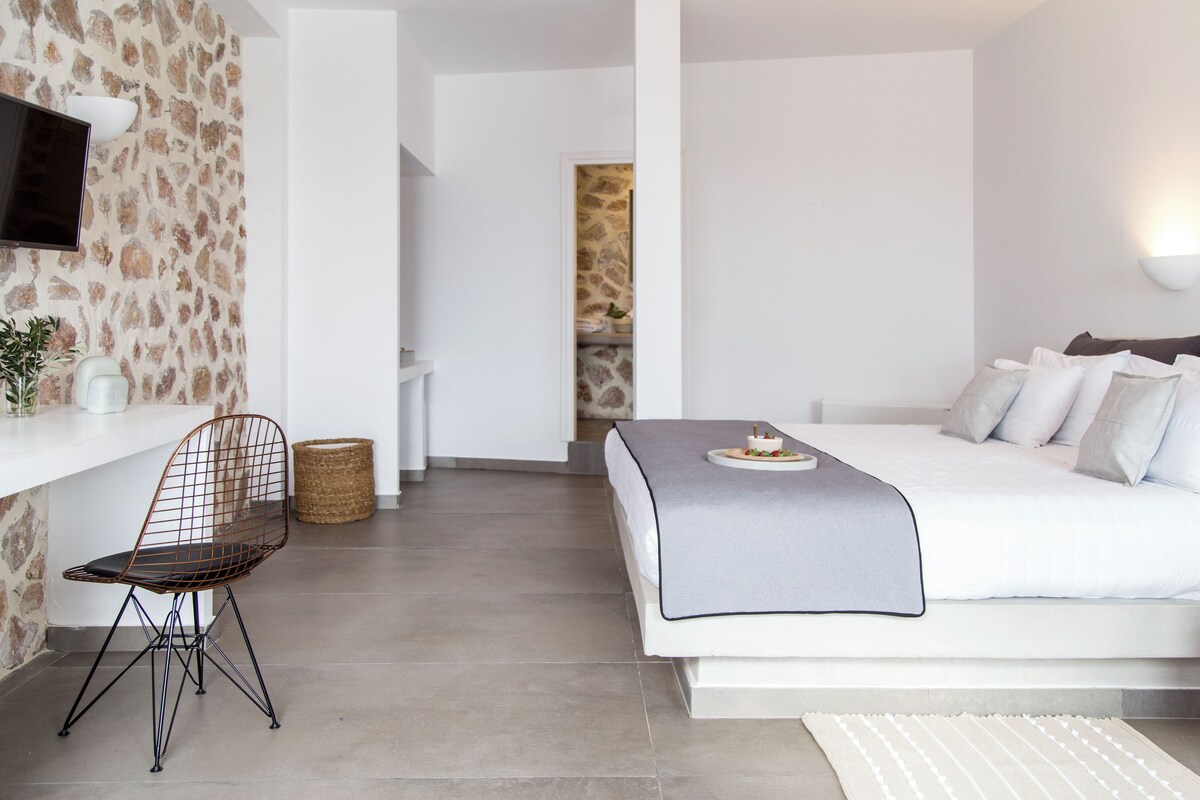 A modern bedroom with a bed, a desk, a chair, and a television.