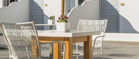 A table with four chairs, a thatched umbrella, and a vase with flowers.
