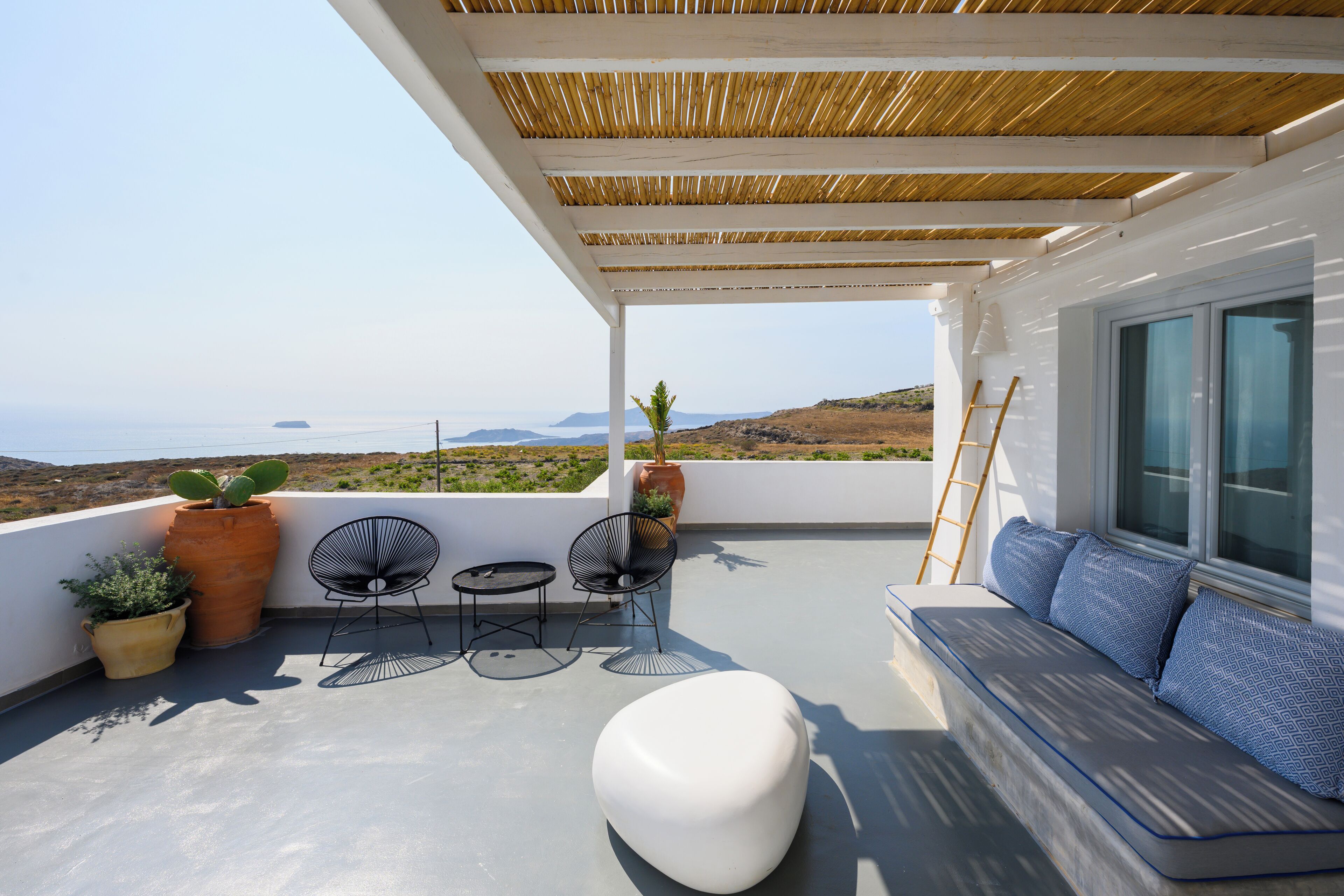 Ein Balkon mit einer weißen Couch, zwei Stühlen, einem kleinen Tisch und Topfpflanzen.