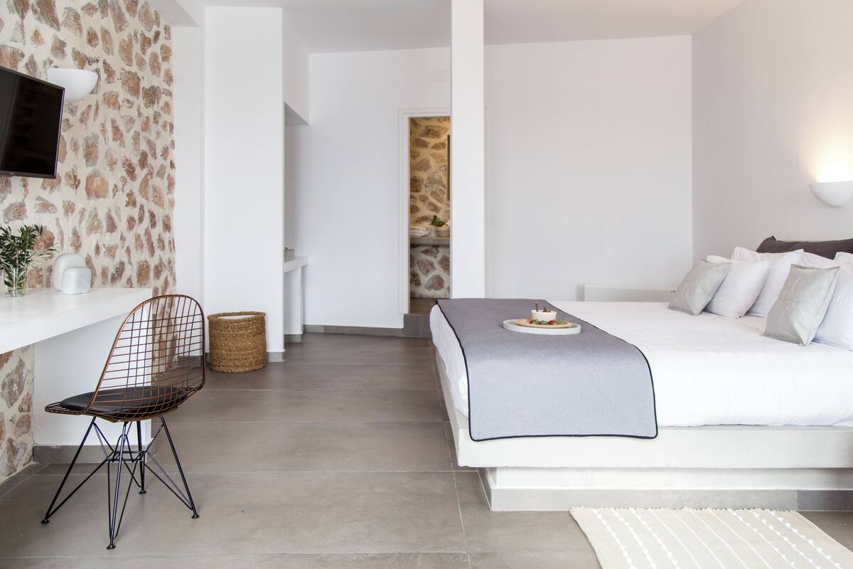 A modern bedroom with a bed, a desk, a chair, and a television.