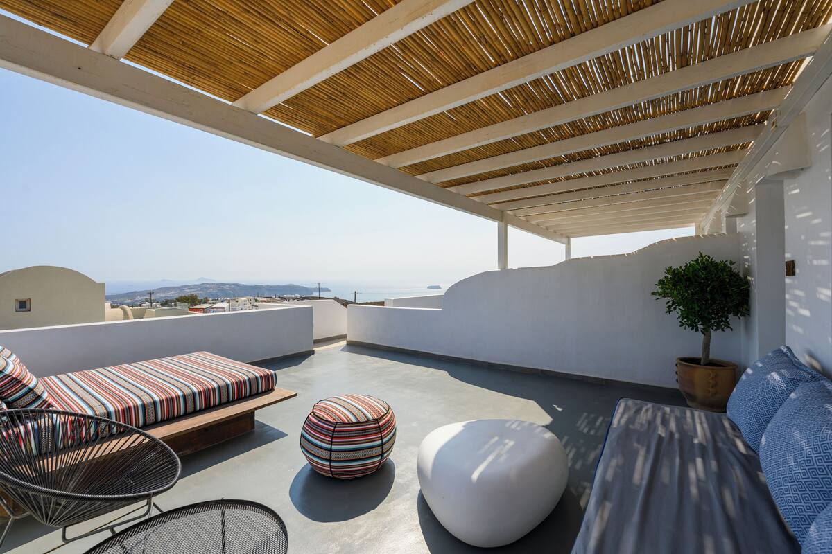 A rooftop terrace with a wooden pergola, a sofa set, a round ottoman, and a potted plant.
