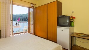 A bedroom with a bed, a wardrobe, a small TV on a mini-fridge, and a table with flowers. - Villa Malfi (Dubrovnik)