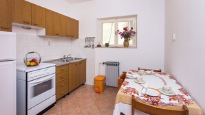 A compact kitchen with wooden cabinets, a white stove, and a dining table set for four. - Villa Malfi (Dubrovnik)