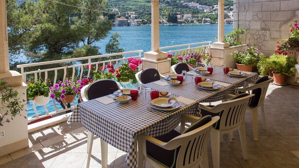 A terrace with checkered tablecloths, white chairs, and potted plants. - Villa Malfi (Dubrovnik)