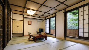 Une pièce de style japonais traditionnel, avec un sol recouvert de tatamis, une table basse, un téléviseur et des portes coulissantes donnant sur un paysage verdoyant.