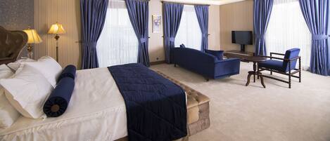 A hotel room with a bed, a sofa, a chair, a TV, and curtains.