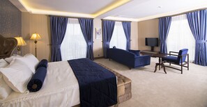 A hotel room with a bed, a sofa, a chair, a TV, and curtains.