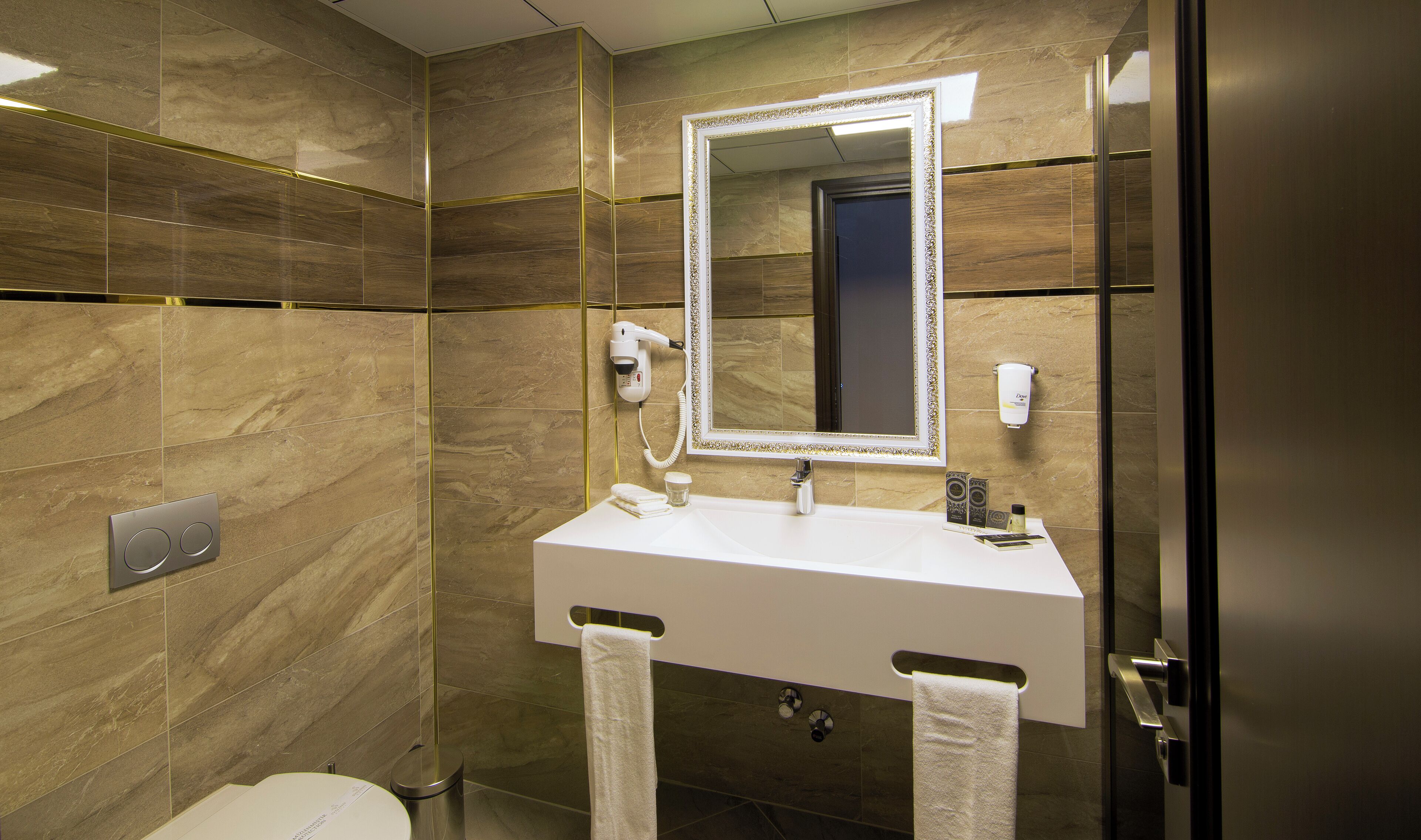 A modern bathroom with a marble wall, a large mirror, a sink, and a hairdryer mounted on the wall.