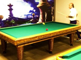 A pool table with a green felt surface, wooden legs, and a yellow cue stick.