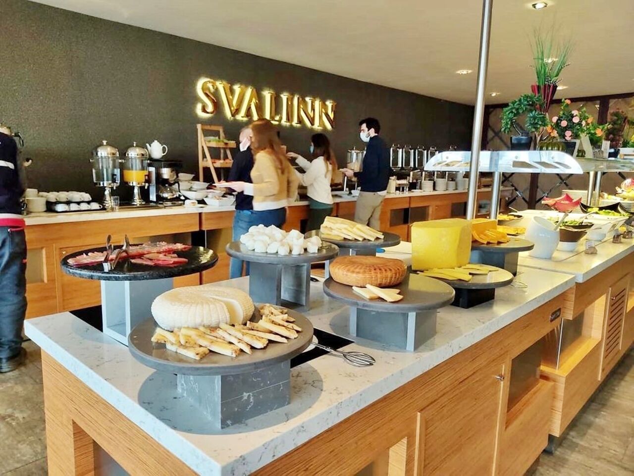 Un montaje tipo bufé con diversas opciones de comida y un letrero de neón que dice "SVALINN" al fondo.