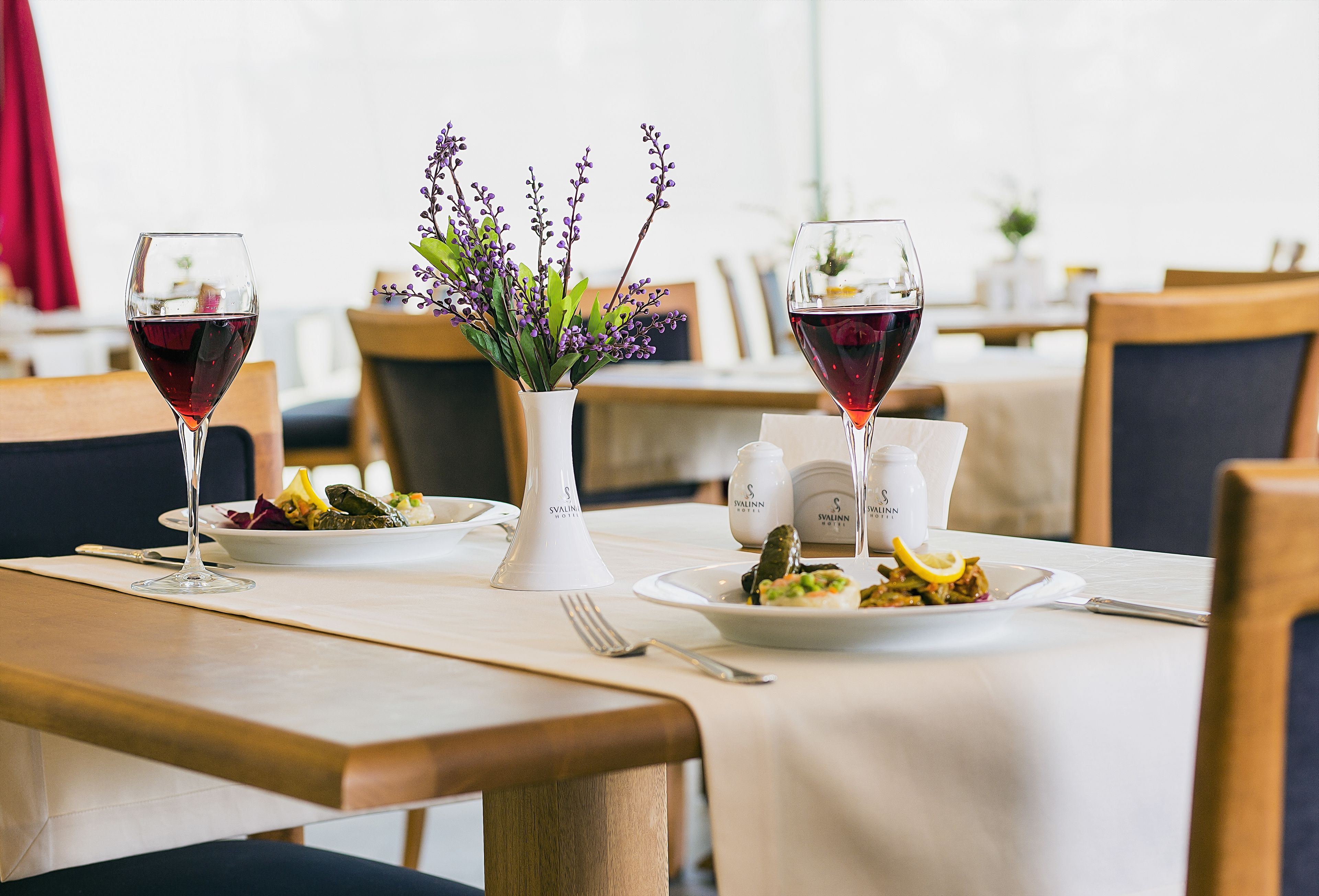Uma mesa de jantar com duas taças de vinho, um vaso com flores e pratos de comida.
