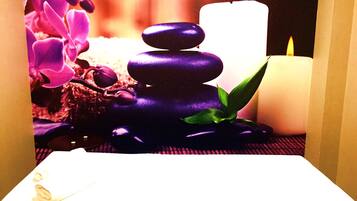 Un área de spa con una composición de piedras, velas y flores moradas.