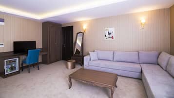 A hotel room with a seating area, a television, a desk, and a minibar.
