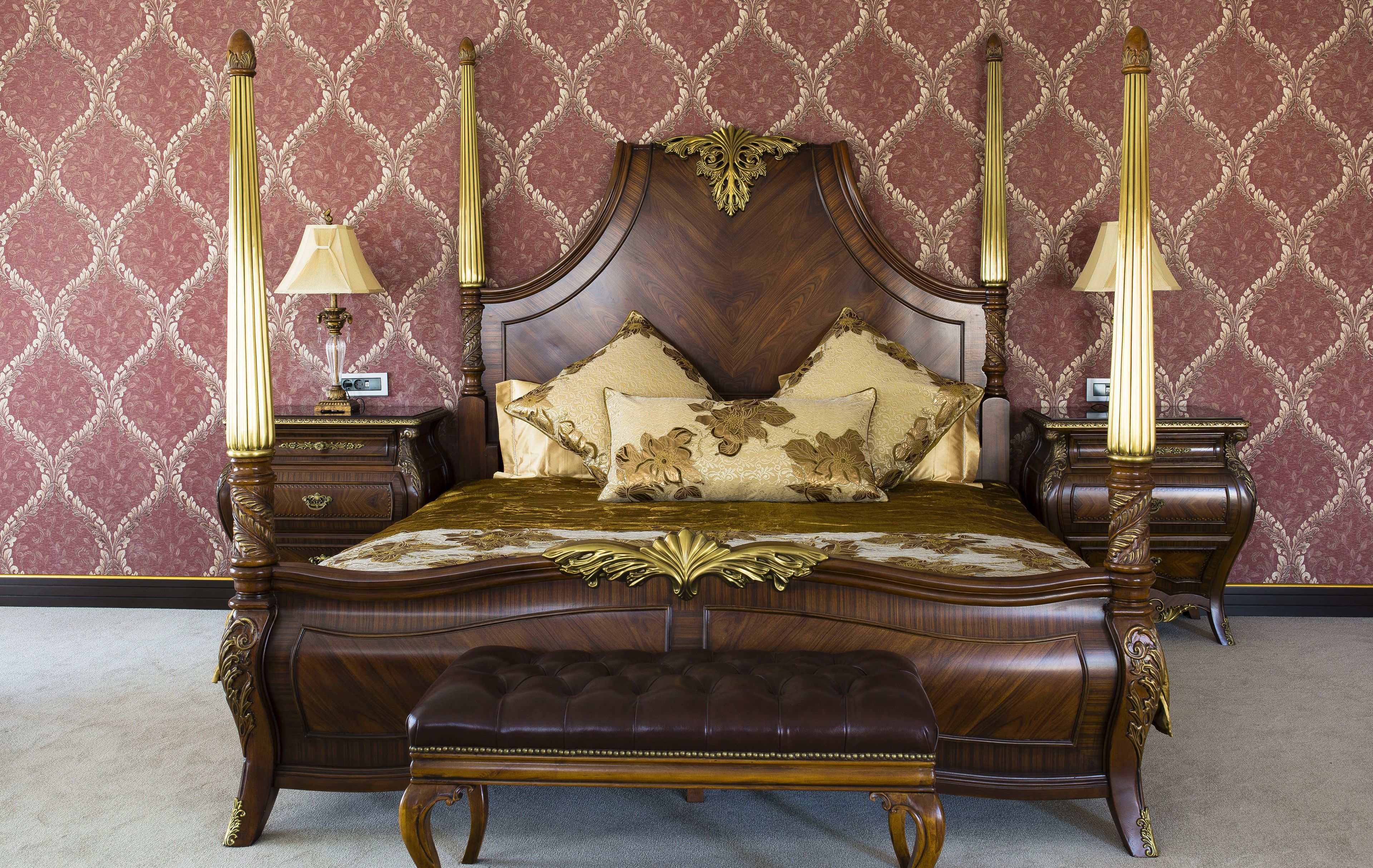 A four-poster bed with a dark wooden frame and gold accents, flanked by two nightstands with lamps.