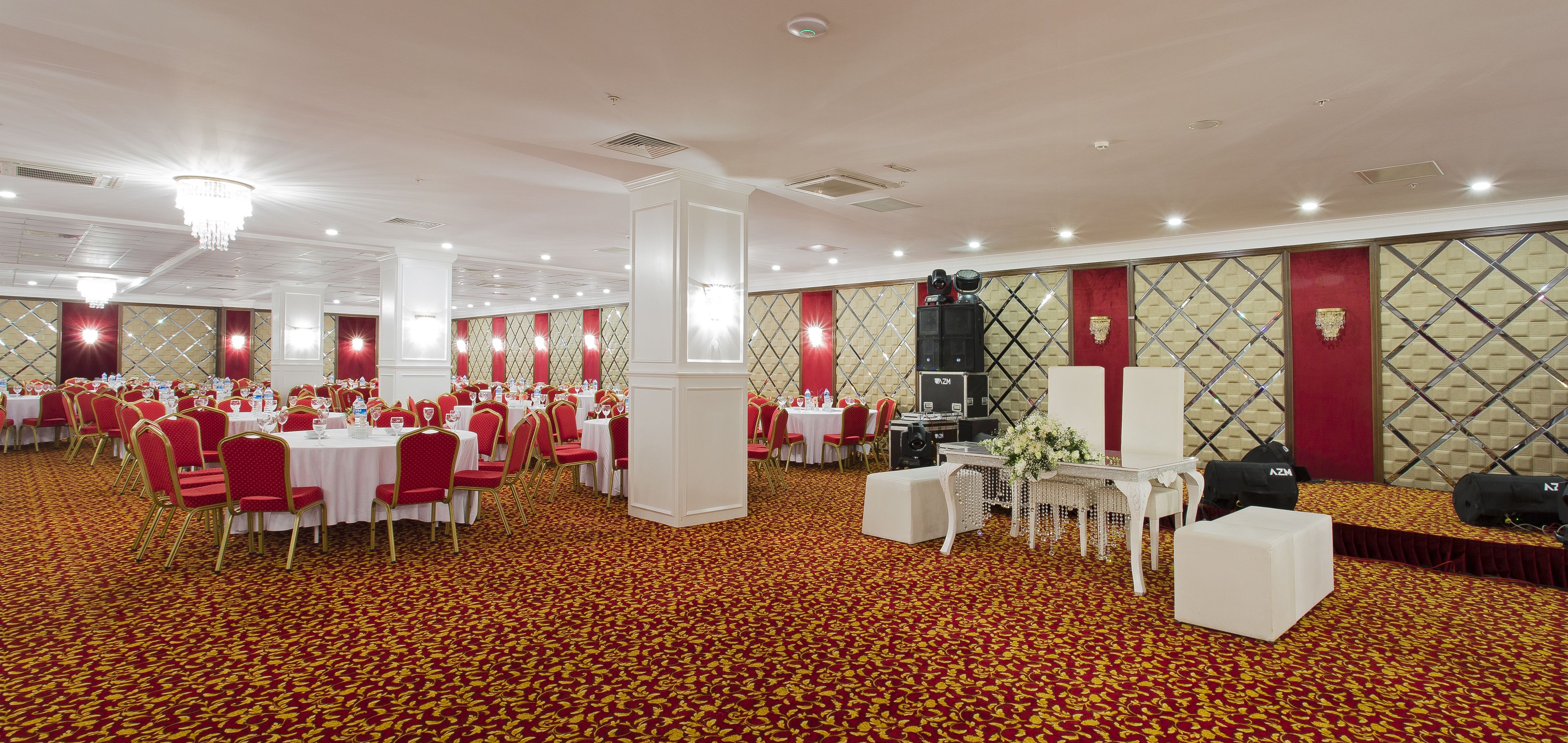 Un salón de banquetes con mesas redondas, sillas rojas y piso cubierto de alfombra roja.