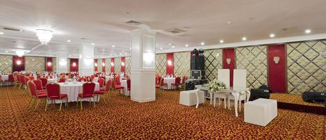 Un salón de banquetes con mesas redondas, sillas rojas y piso cubierto de alfombra roja.