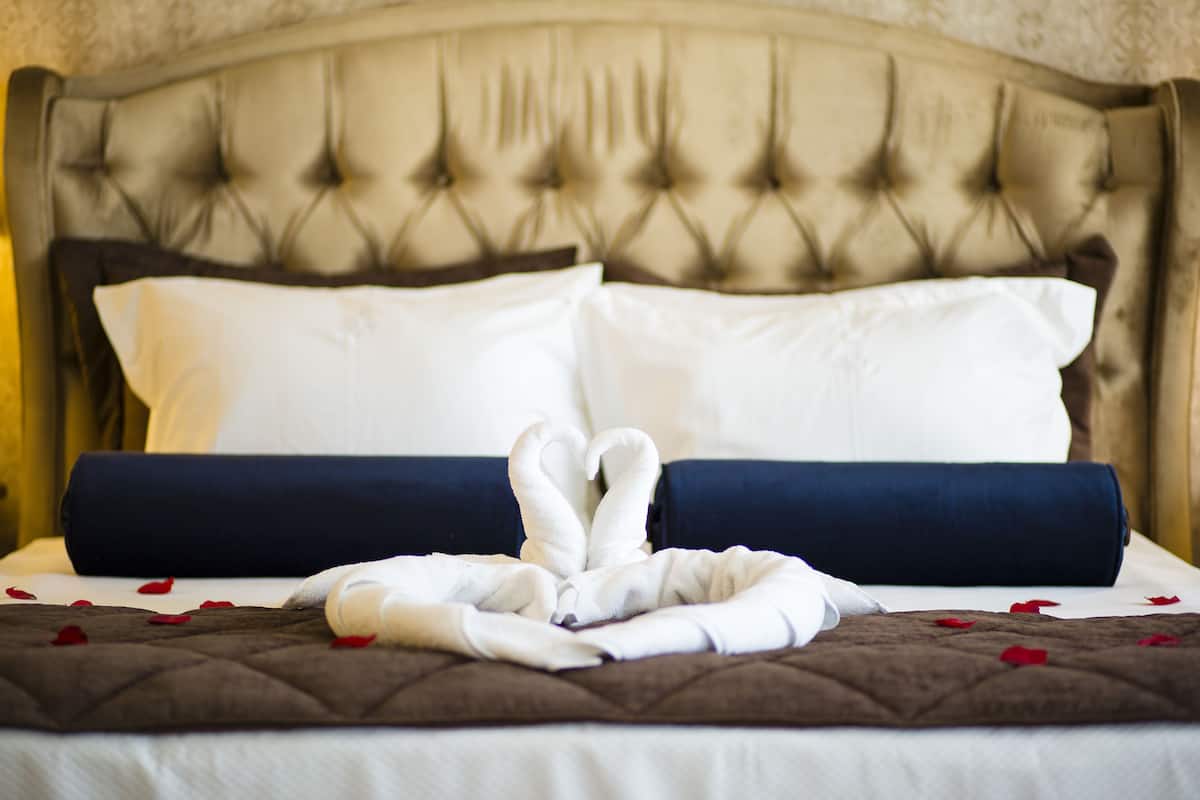 Una cama bien hecha con un edredón marrón, almohadas blancas y un cojín decorativo azul.