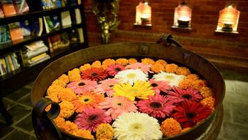 Una olla metálica grande llena de flores coloridas, una estantería con libros y apliques decorativos en la pared.