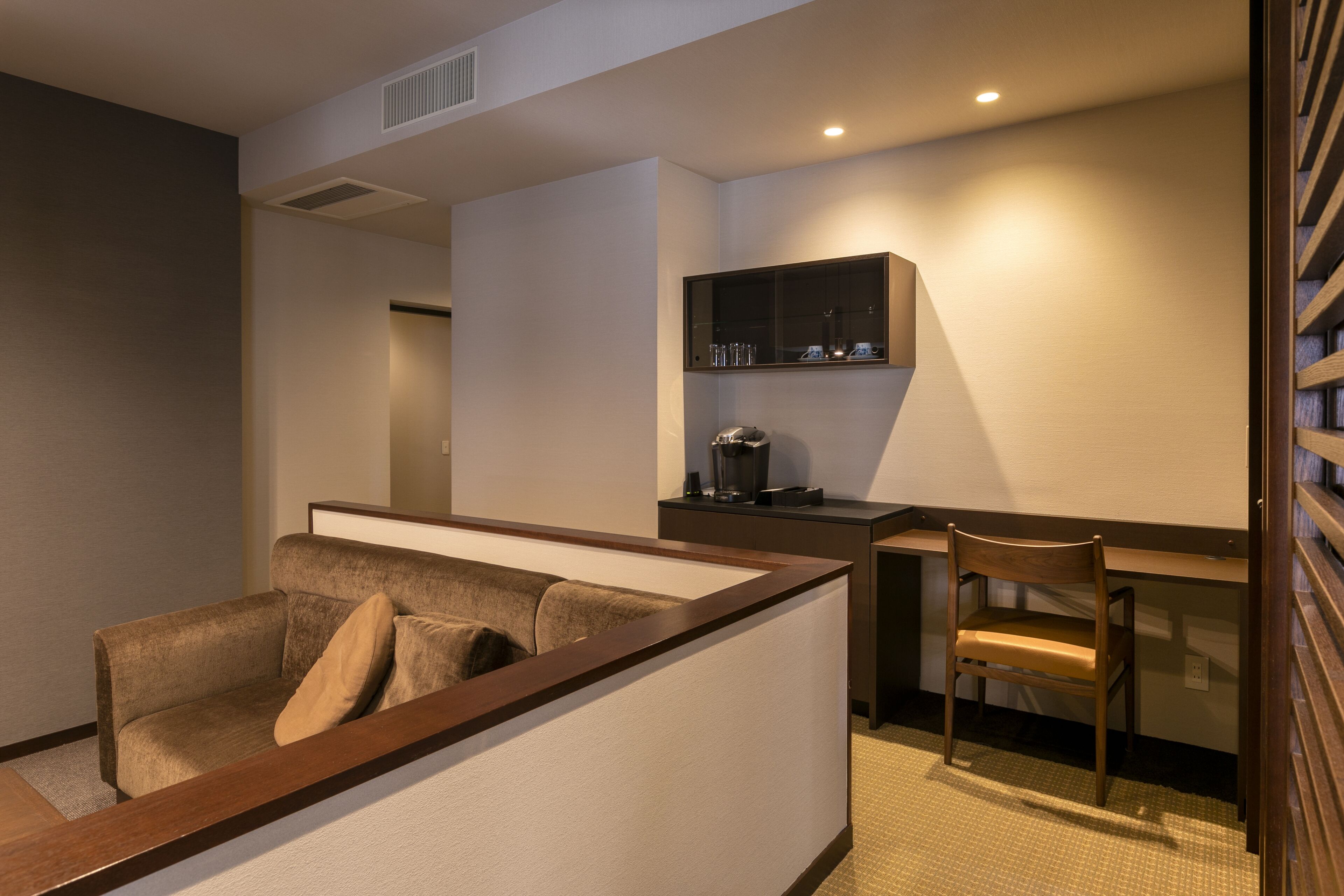 Una habitación de hotel moderna con sofá, escritorio de madera, una silla y un armario empotrado.