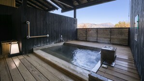 A wooden deck with a hot tub, a wooden wall, and a view of mountains.