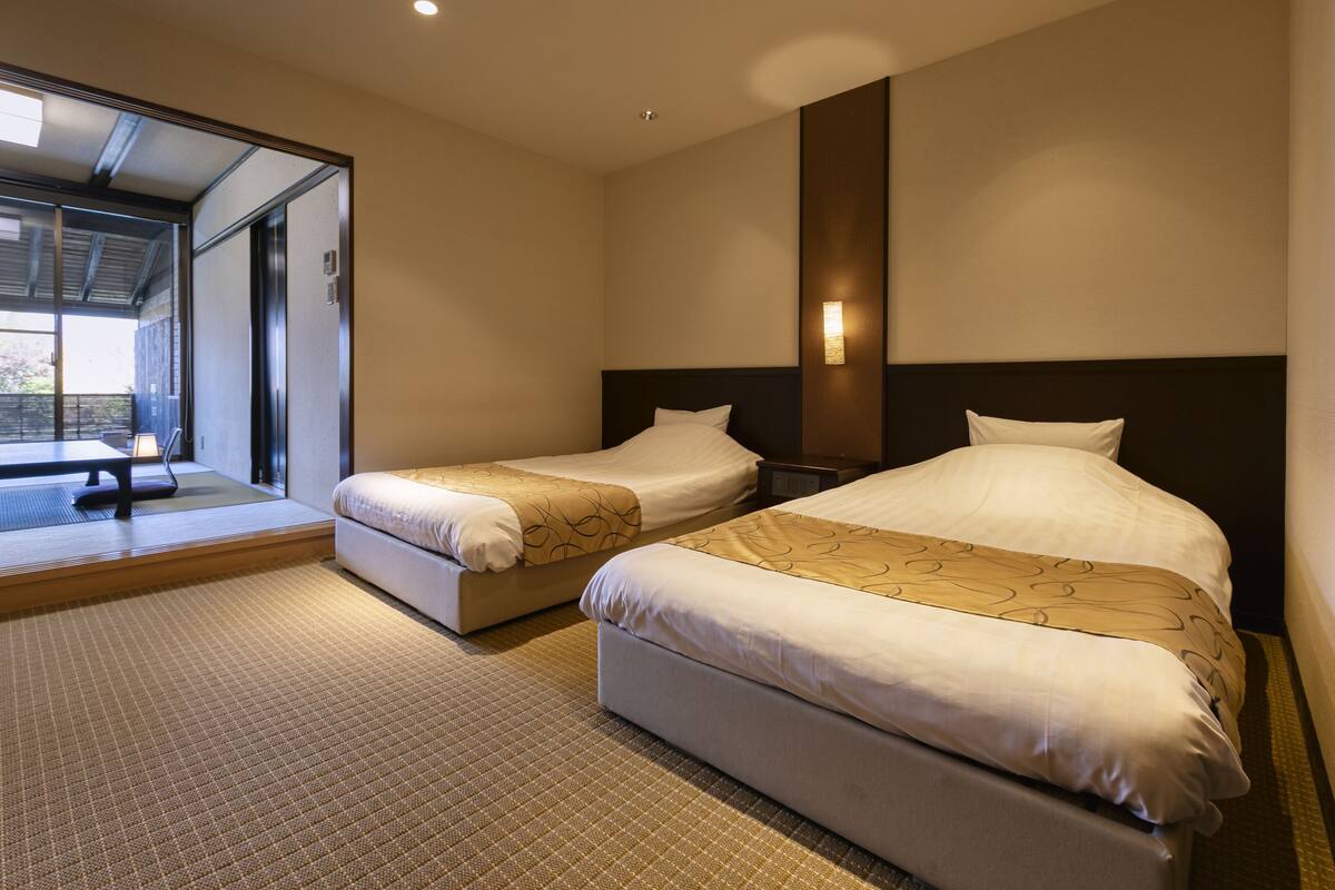 A hotel room with two beds, a sitting area with a bench, and a view of the outdoors.