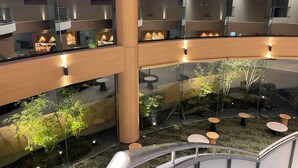 A modern atrium with glass walls, wooden beams, and a central garden area with tables and chairs.