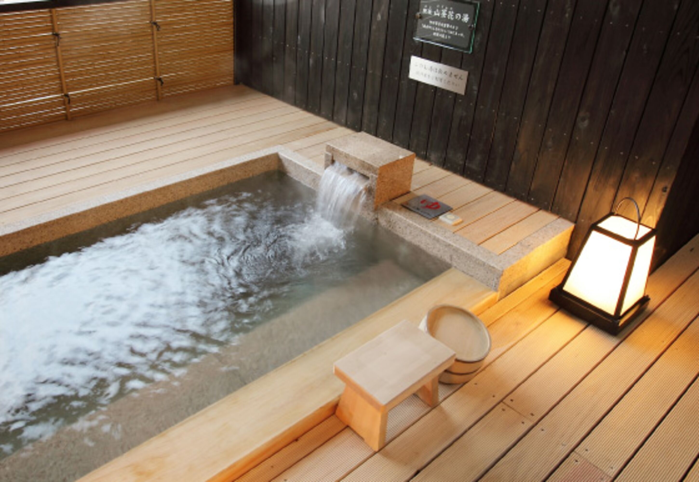 A wooden deck with a hot spring, a wooden bench, and a lantern.