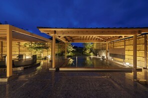 Un área de piscina exterior techada con una pérgola de madera, piso de piedra y un espacio de descanso con jacuzzi.