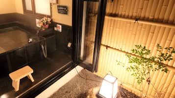 Una habitación al estilo japonés tradicional, con suelo de tatami, un taburete de madera, un lavabo y una pequeña planta.
