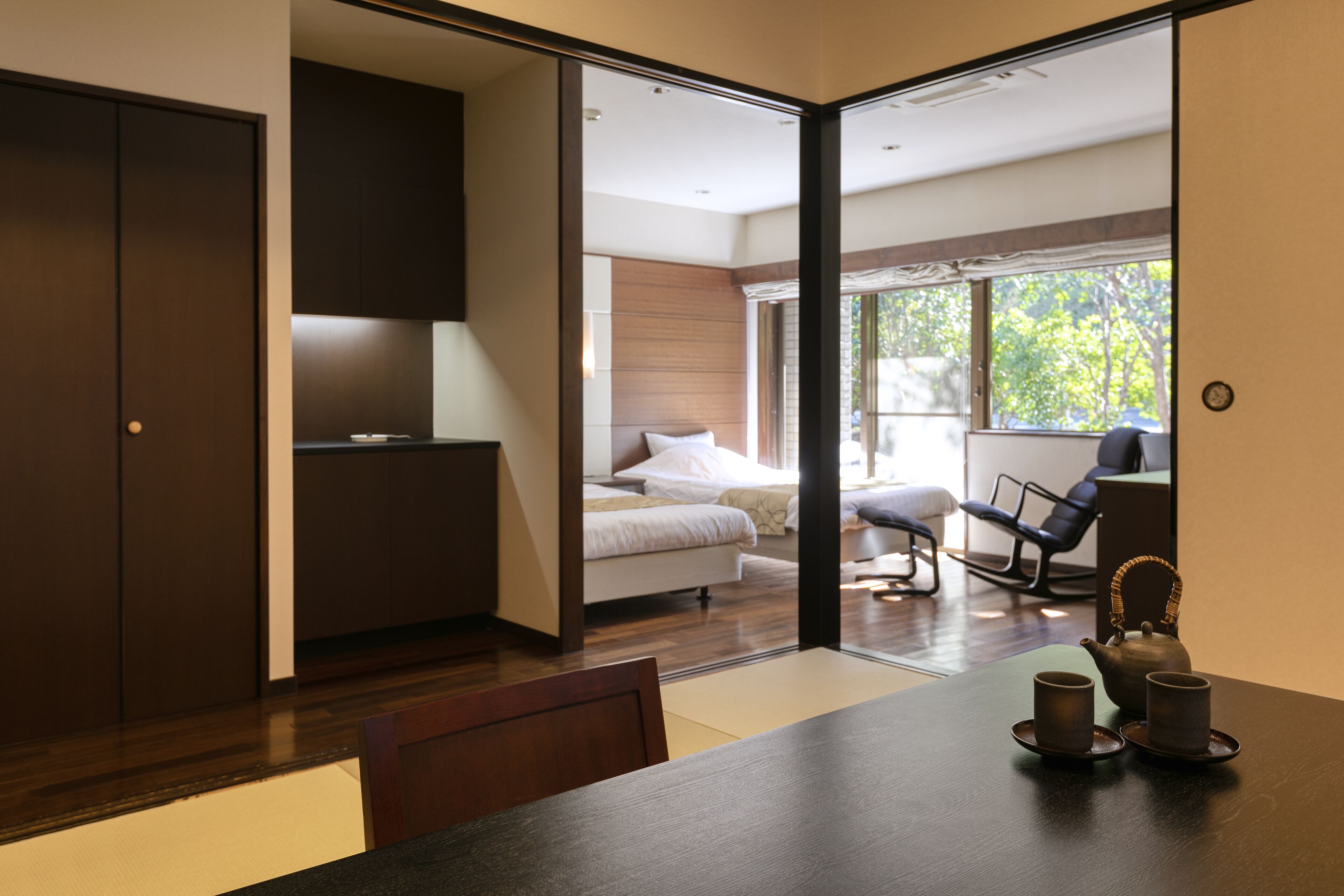 Una habitación de hotel moderna con una cama, un escritorio, una silla y una mesa de comedor con dos tazas y una tetera.