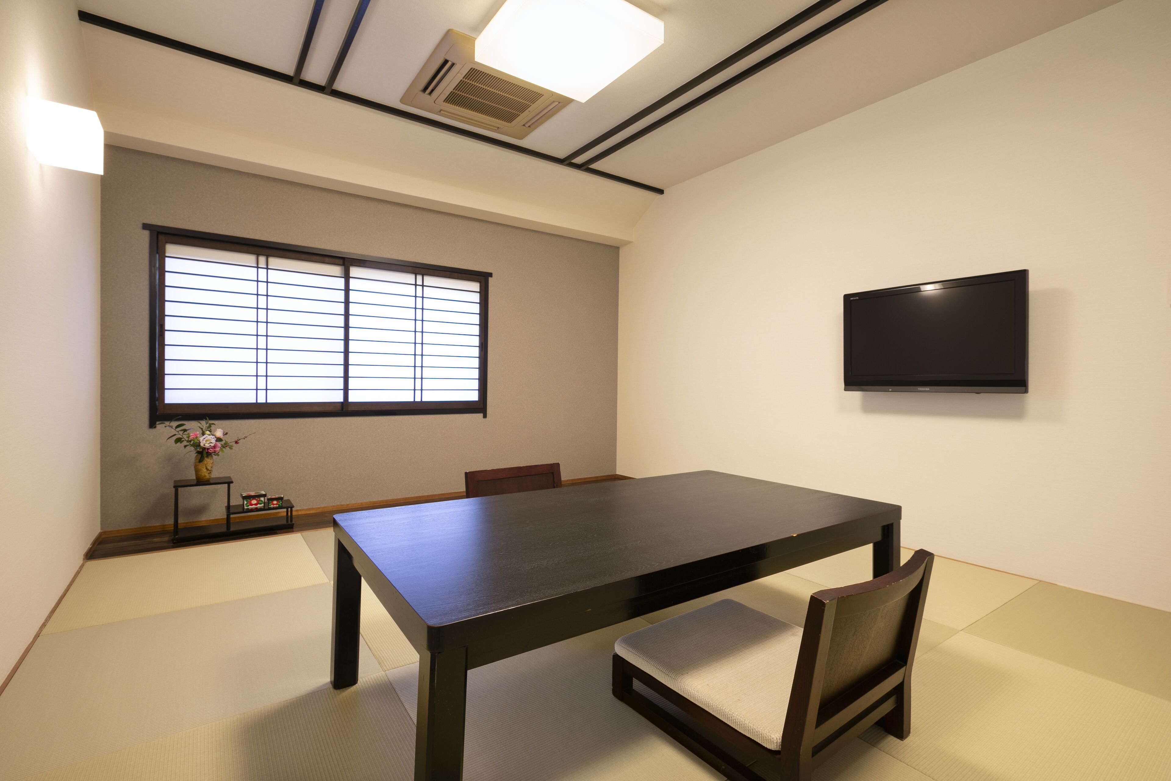 A conference room with a large table, chairs, a TV, and a window with blinds.