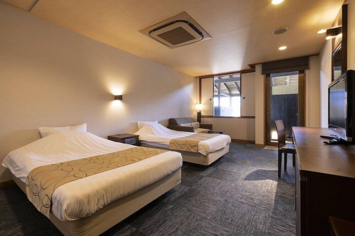 A hotel room with two beds, a desk, a chair, a TV, and a window.
