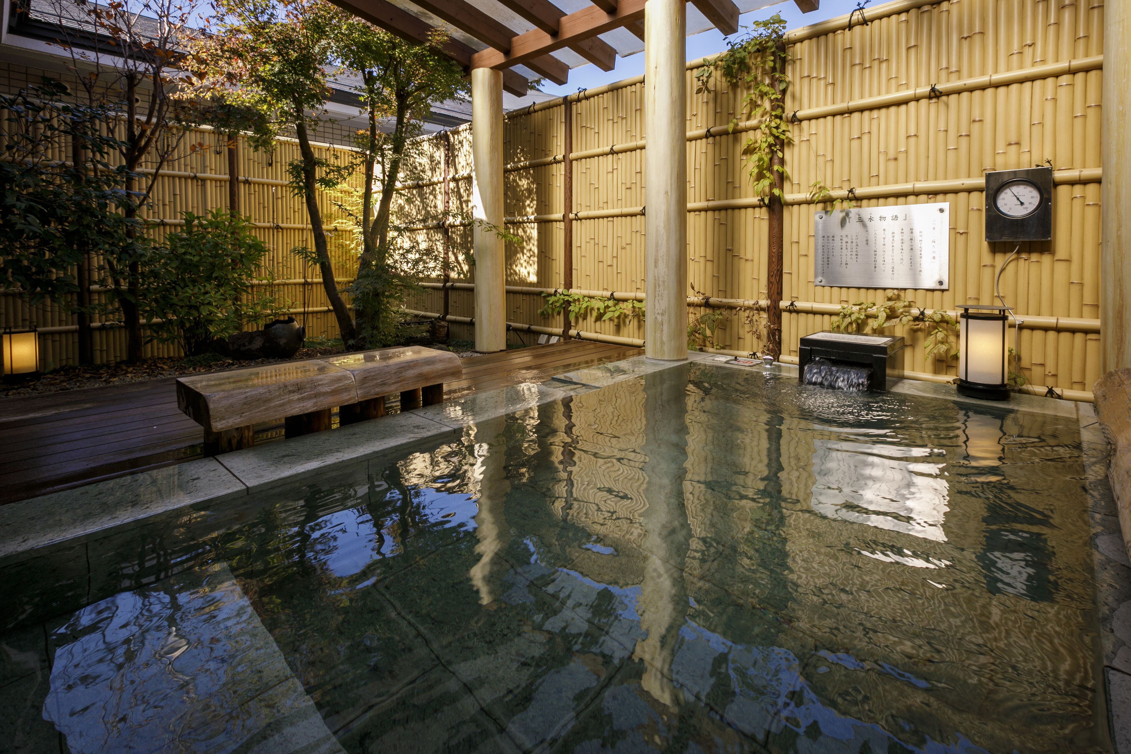 A traditional Japanese onsen with a wooden deck, bamboo walls, and a stone basin.