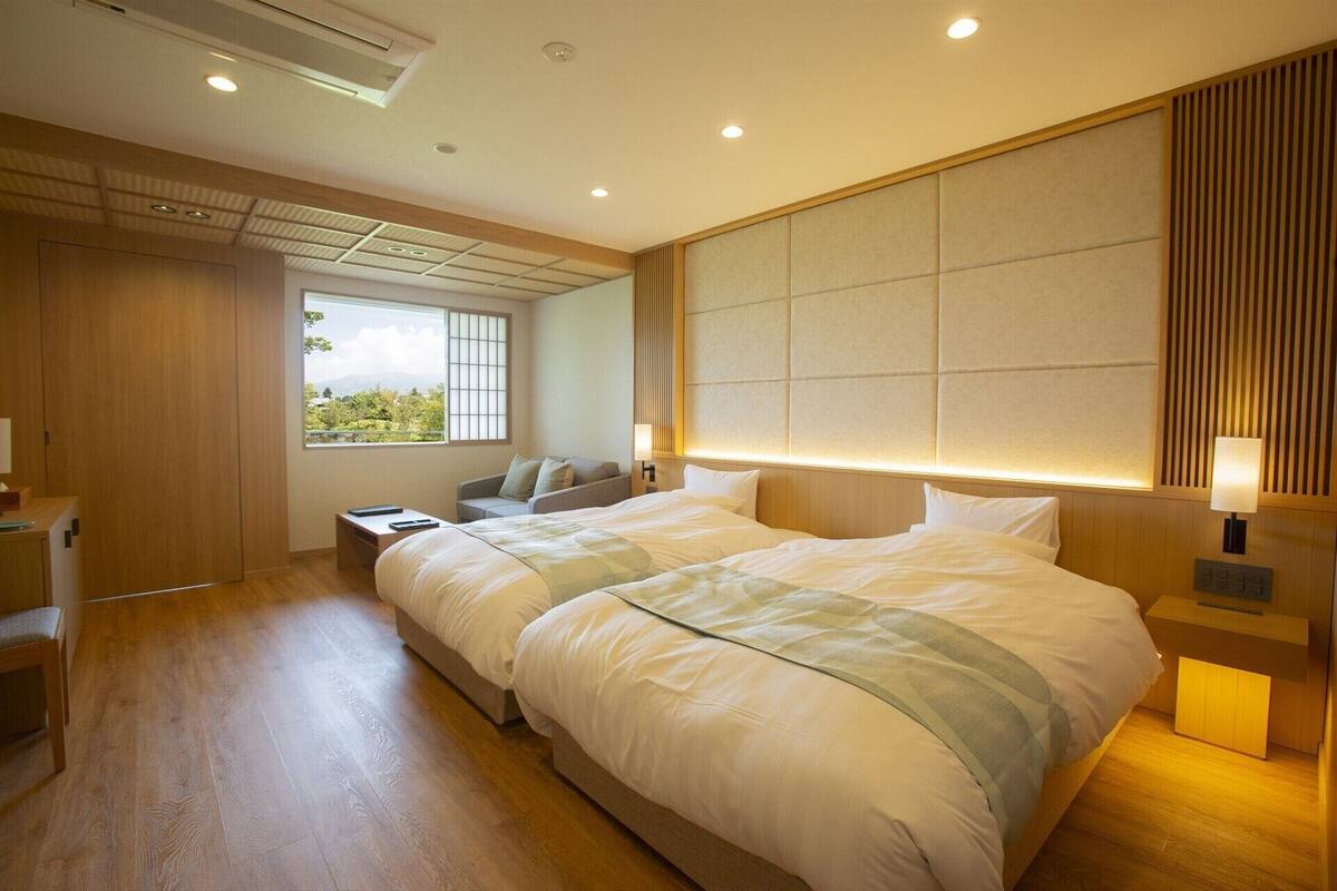A hotel room with a large bed, a desk, a chair, a window with a view, and a wooden headboard.
