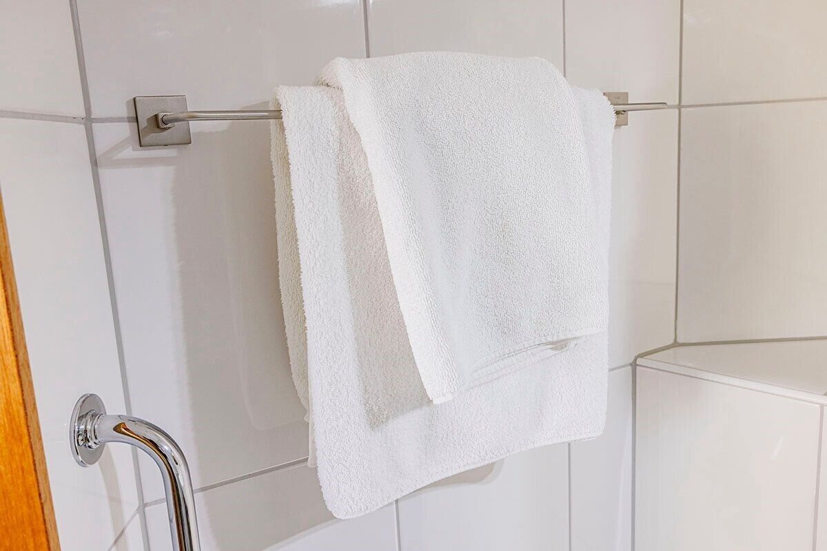 Una toalla blanca colgada en un perchero metálico en un baño con azulejos blancos.