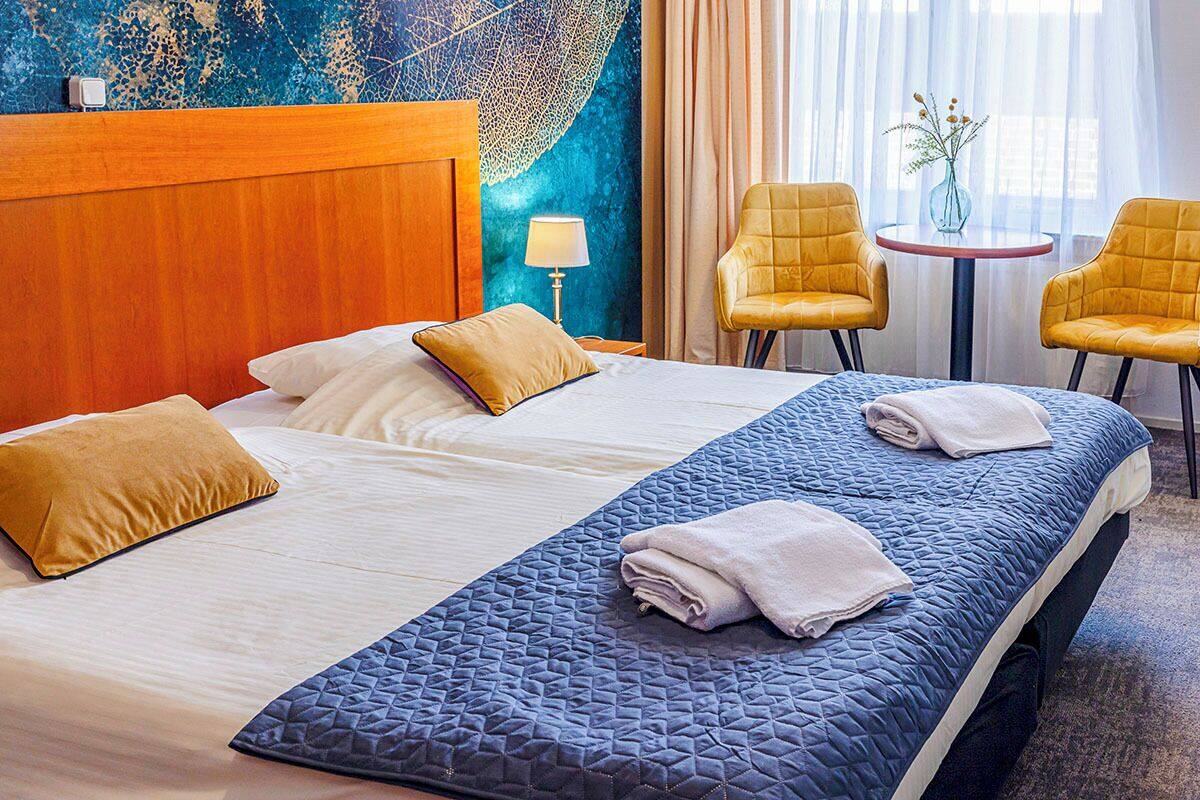 Une chambre d’hôtel avec un grand lit, deux chaises, une petite table et un mur décoratif.