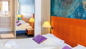 Een hotelkamer met een groot bed, twee bedlampjes, een houten hoofdeinde en een badkamer die door een open deur zichtbaar is.
