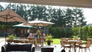Een terras buiten met rieten meubels, parasols en potplanten.