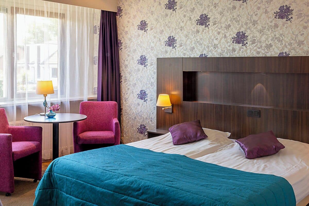 Une chambre d’hôtel avec un lit, deux chaises, une petite table et une lampe.