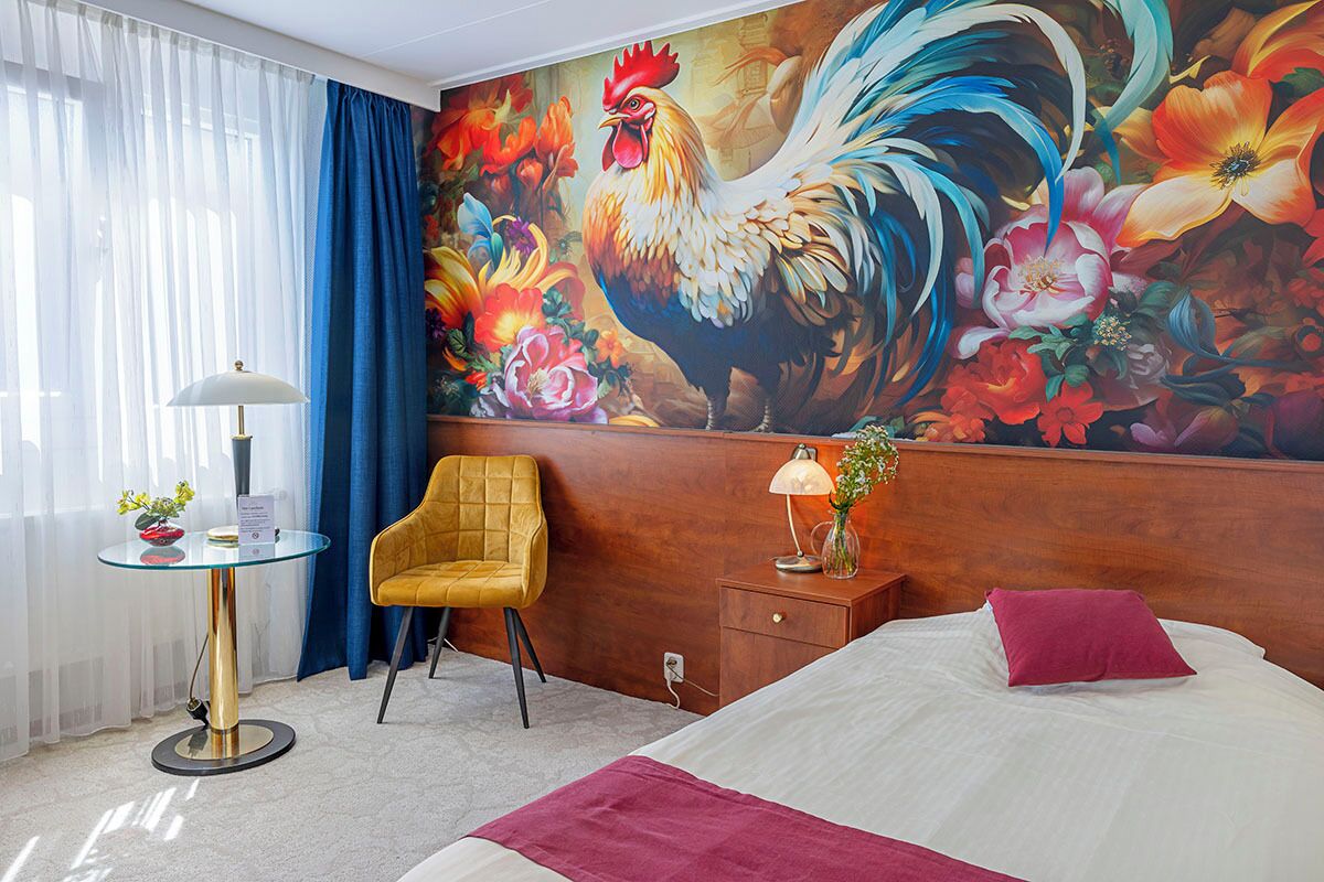 Hotelkamer met een bed, een stoel, een tafel met een lamp en een grote bloemenmuur.