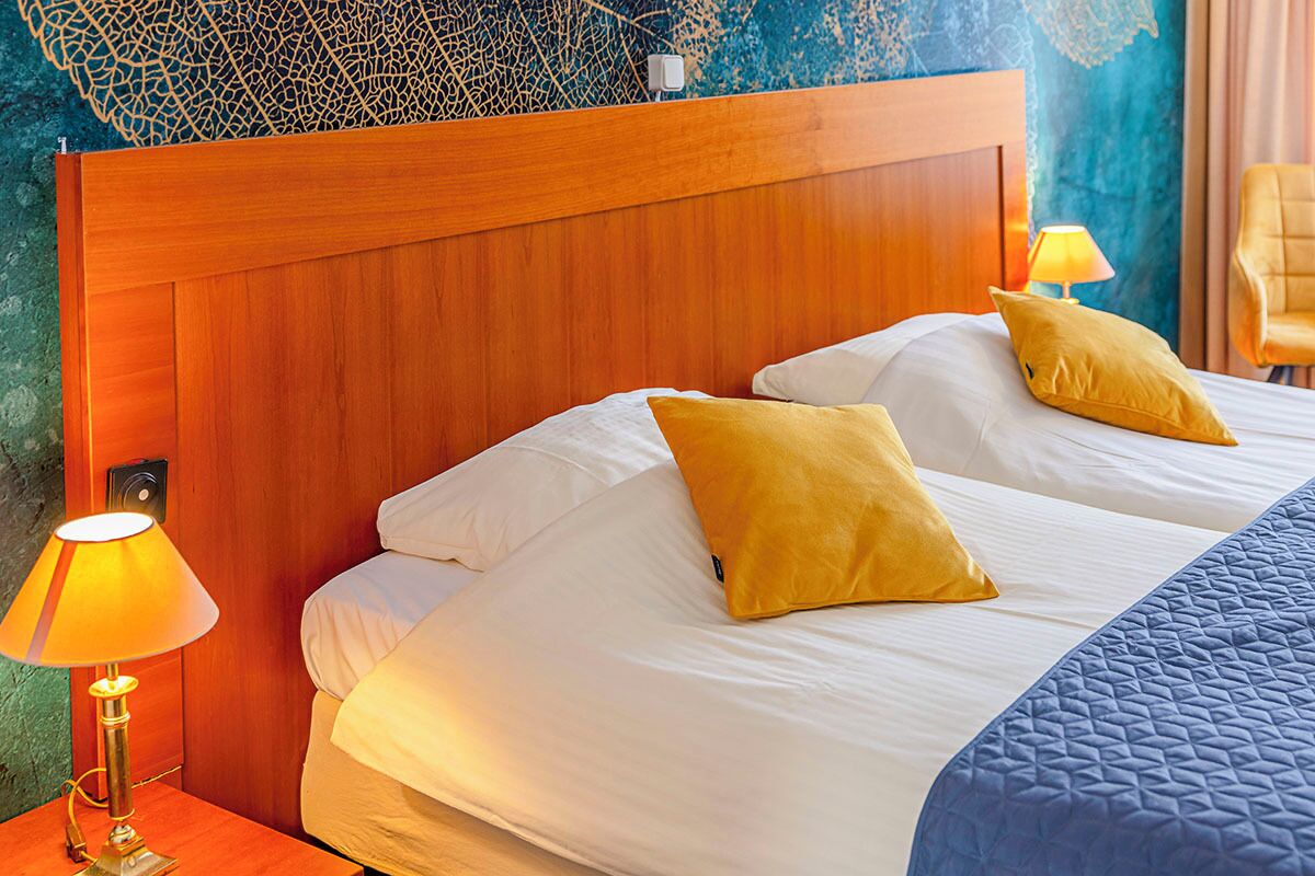A double bed with white linens and two yellow pillows, a wooden headboard, and a nightstand with a lamp.