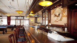 Een bar met een lange toonbank, meerdere stoelen en een pooltafel.