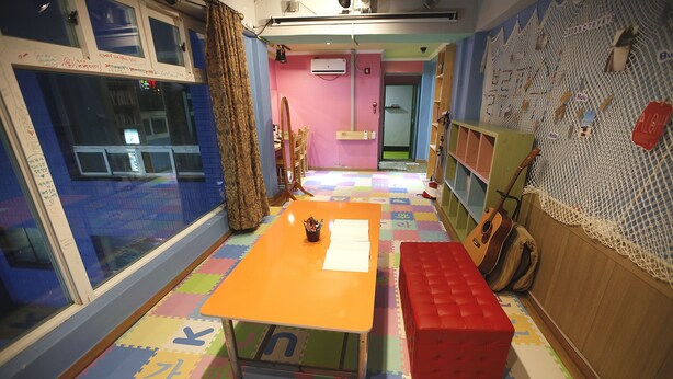 A room with a colorful play mat, a small table with papers, a red bench, and a guitar leaning against the wall. - Bluefish Guesthouse - Hostel (Busan)